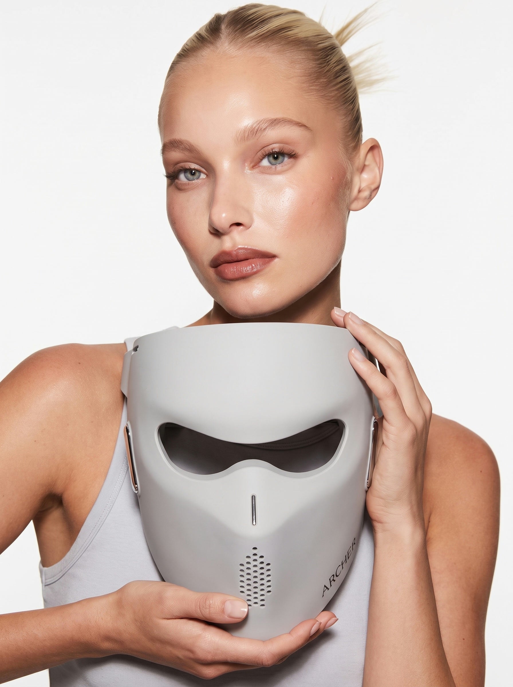Model holding the grey ARCHER LED face mask to her face in soft studio light.
